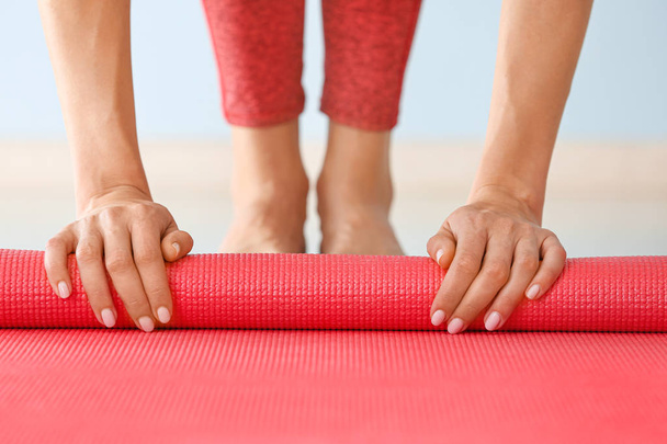Молодая женщина катит коврик для йоги в спортзале, крупным планом
 - Фото, изображение