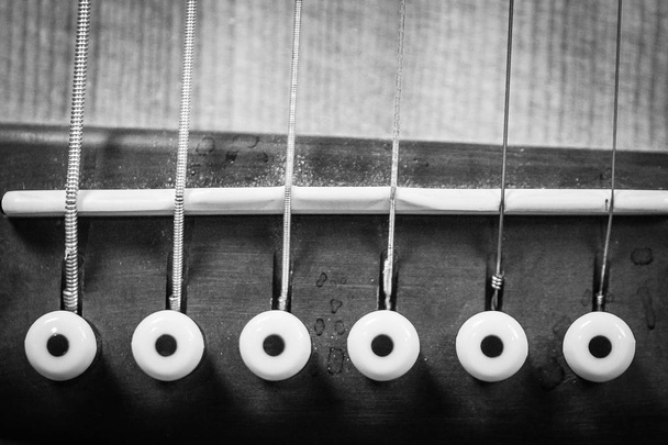 Grayscale closeup of an acoustic guitar's bridge pins and the saddle - 写真・画像