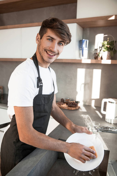 attractive young man is washing dishes in his kitchen - Foto, immagini