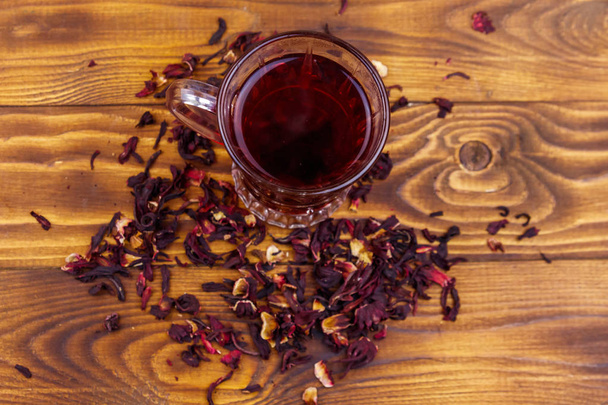 Γυάλινο φλιτζάνι κόκκινο τσάι ιβίσκου (καρκέιντ, ροδοσέλ) σε ξύλινο τραπέζι - Φωτογραφία, εικόνα