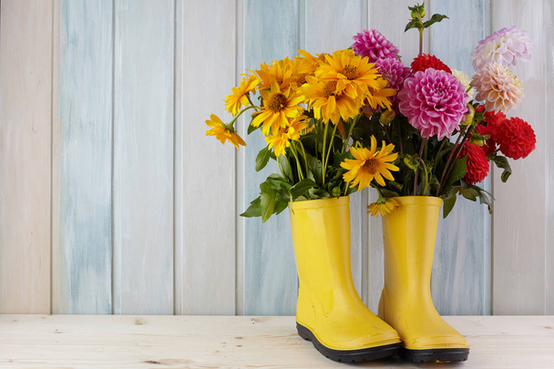 Gele rubberen laarzen staande op een houten achtergrond van vuil en een bloem binnen - Foto, afbeelding