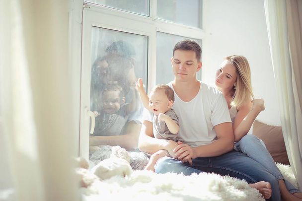 mom dad and baby little toddler sitting on the window / young family in a new apartment, beautiful housing - Foto, afbeelding