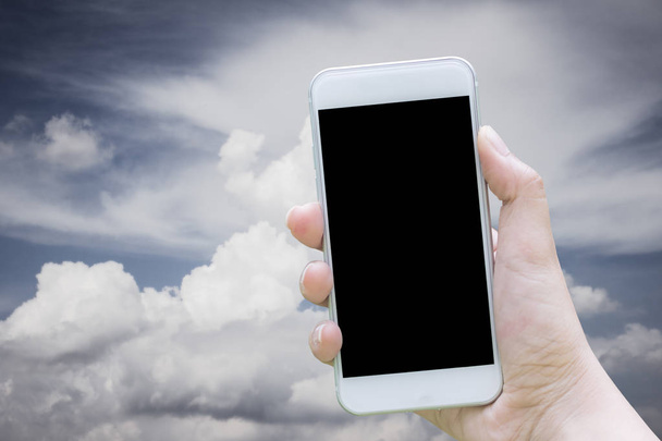 Attrappe des weißen Mobiltelefons, das in der Hand hält, und leerer schwarzer Bildschirm, der Himmel mit Wolken sind auf dem Hintergrund verschwommen. - Foto, Bild