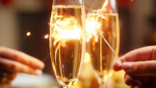 CLoseup Images 4k de jeune homme et femme amoureux tenant deux étincelles brûlantes sur la table avec des verres de champagne pétillant. Famille célébrant Noël et le Nouvel An
 - Séquence, vidéo
