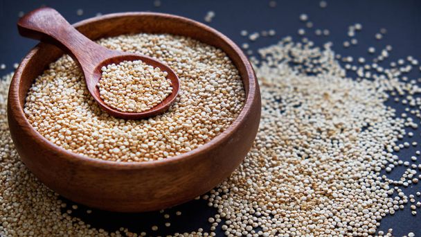 weiße Quinoa-Samen auf schwarzem Hintergrund. Quinoa in Schüssel und einem Löffel auf dem Küchentisch Ansicht. gesunde und ernährungsbewusste Superfood-Produkte. - Foto, Bild