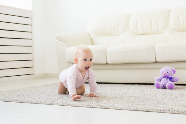 Adorable baby girl learning to crawl in white sunny room. - Photo, Image