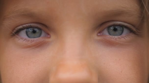Blauwe ogen van mooie kleine meid knipperen en kijken naar de camera met een triest gezicht. Portret van een schattig gezicht van jong kind kijken met een bedroefd uitdrukking. Close-up - Video