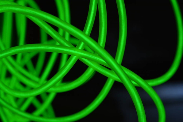 異なる形状および構造を有する有毒な緑色の発光電発光ワイヤー。黒い光沢のある表面に位置する石灰エレクトロルミネッセンス繊維、エルワイヤー、珍しい円のウェブ. - 写真・画像