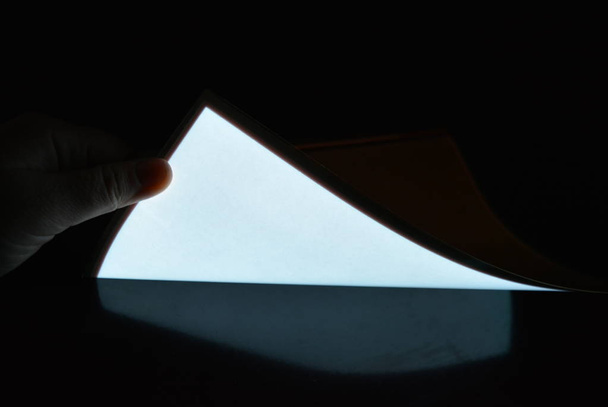 Very bright and luminous A4 electroluminescent paper with an  coating is located in different flatnesses on a pristine glossy surface with a female hand. Excellent color substrate, uniform glow. - Фото, зображення