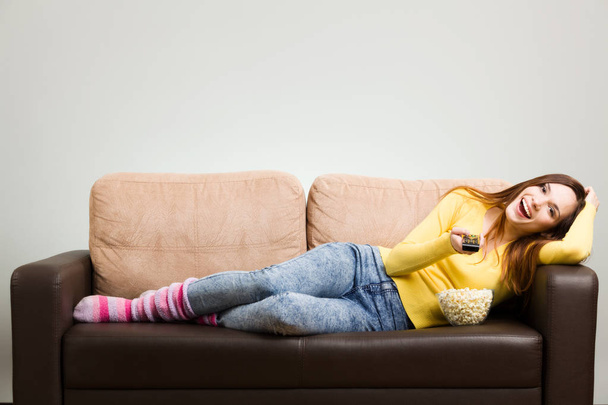 Young woman spends his free time watching TV on the couch at hom - Foto, Bild