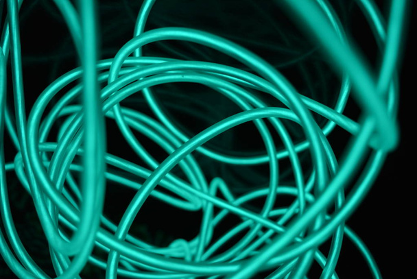 Unusual bright wires made of turquoise-colored material glowing at night. Chaotic sky blue wires, light guide electroluminescent wires, electroluminescence are located on a glossy black surface. - Photo, Image