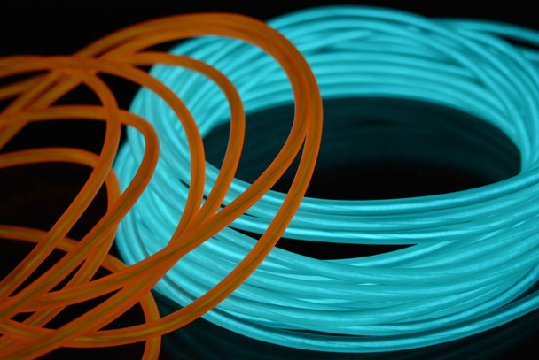 Une bobine lumineuse de fil lumineux bleu ciel turquoise avec des fils chaotiques d'un guide de lumière orange situé sur une surface noire brillante. Toile légère, rétroéclairage avec fils et fond d'art
. - Photo, image