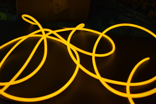 Filo luminoso arancione brillante, filo di luce ritorto, cavo. Diverse forme e immagini di fili lectroluminescenti con diverse torsioni, succosa el filo
. - Foto, immagini