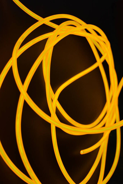 leuchtend orangefarbener Leuchtdraht, gedrehter Lichtdraht, Kabel. verschiedene Formen und Bilder von Lectrolumineszenzdrähten mit unterschiedlichen Drehungen, saftige el-Drähte. - Foto, Bild