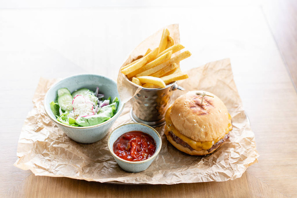 Hamburguesa de queso con lechuga, tomate, papas fritas y queso derretido. La mesa en el restaurante. Alimentos poco saludables
. - Foto, imagen