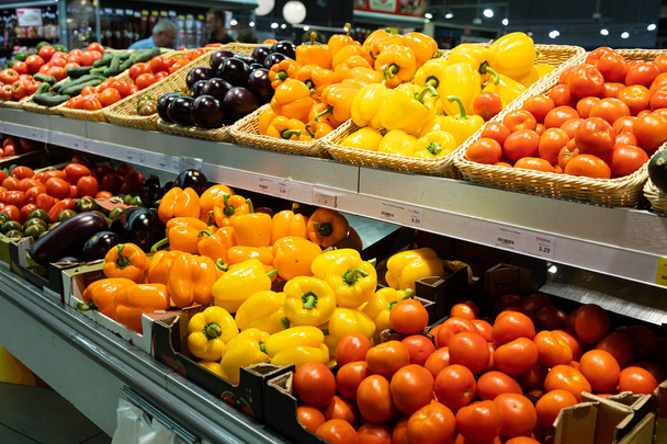 Angular view of supermarket counter with wicker baskets and lug boxes with fresh tomatoes, orange and yellow peppers and eggplants - Photo, Image