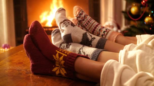 Closeup 4k felvételeket az emberek gyapjú zokni gazdaság láb mellett égő tüzet kandalló éjjel. Az emberek pihennek a téli ünnepek és ünnepségek otthon - Felvétel, videó