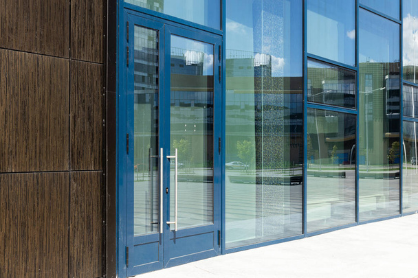 Θέα από το σύγχρονο τοίχο του κτηρίου με γυάλινο παράθυρο και πόρτα με μπλε κορνίζα. Αντανάκλαση του δρόμου - Φωτογραφία, εικόνα