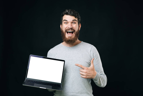 Foto di un uomo barbuto eccitato in casuale che punta lo schermo vuoto sul suo computer portatile
 - Foto, immagini