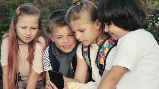 Plezier met telefoon. Twee kleine schoolmeisjes en twee jongens met behulp van slimme telefoon. - Video