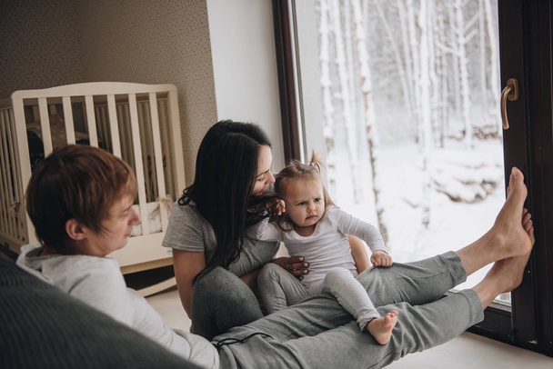 The family is sitting at the window and looking at the winter forest. Good New Year spirit. Morning in pajamas. - Fotó, kép