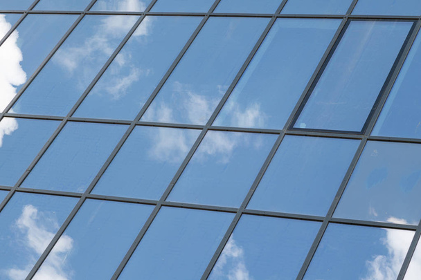 Γωνιακή θέα του σύγχρονου γυαλιού κτίριο με ουρανό αντανάκλαση στα παράθυρα. - Φωτογραφία, εικόνα