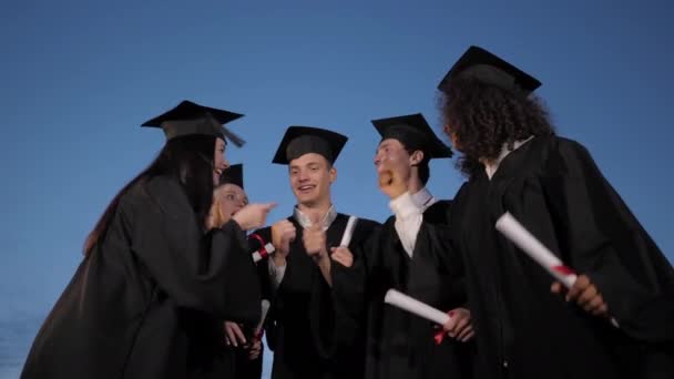 卒業式の日に学生の友人の幸せと興奮のグループは、夕方に空気中に彼らの帽子を投げます. - 映像、動画