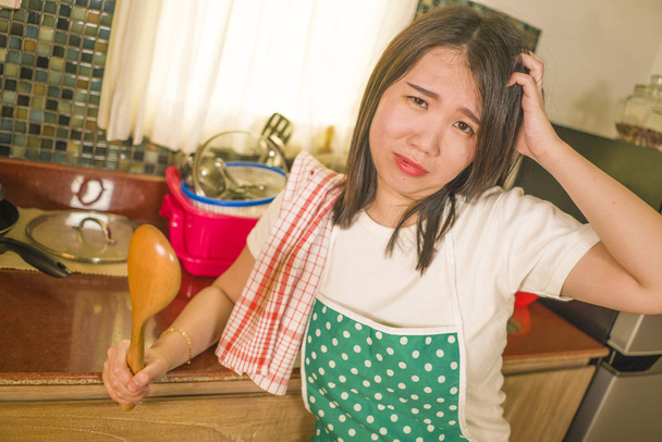 young tired and stressed Asian Chinese woman in cook apron working leaning on kitchen sink lazy in moody and upset face housekeeping at home and crying - Foto, Imagen
