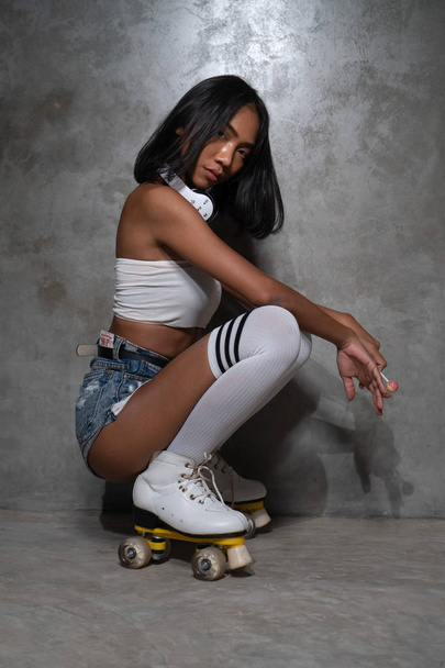 Young beautiful Asian girl in retro quads roller skates posing in studio over concrete wall background - Φωτογραφία, εικόνα