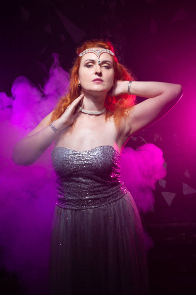 Mature plus size red hair woman in grey evening dress posing on dark smoke background ready for halloween. - Photo, Image