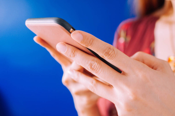 Μια νεαρή γυναίκα χρησιμοποιεί ένα κινητό τηλέφωνο σε μπλε φόντο - Φωτογραφία, εικόνα