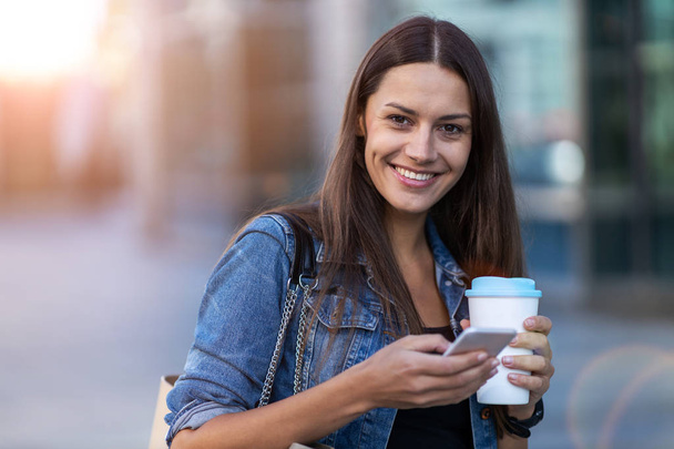 Молодая женщина со смартфоном и кофе в городе
  - Фото, изображение