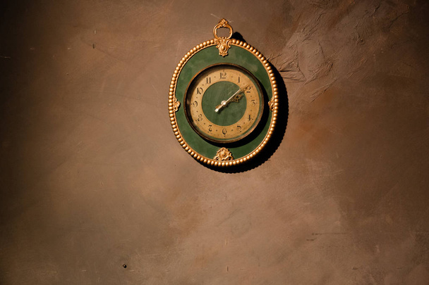 Gold vintage clock with arabic numbers. Beautiful green frame clock hanging on the brown wall. Antique round wall timepiece. Copyspace - Zdjęcie, obraz