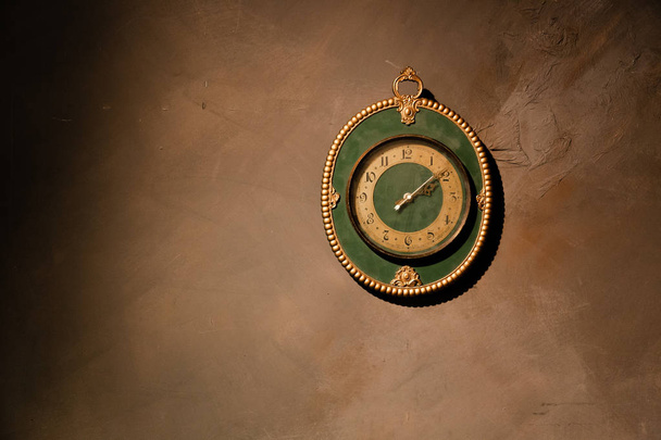 Gold vintage clock with arabic numbers. Beautiful green frame clock hanging on the brown wall. Antique round wall timepiece. Copyspace - Photo, Image