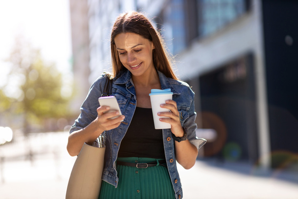 Jonge vrouw met smartphone en koffie in de stad  - Foto, afbeelding