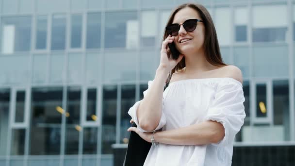 Современная молодая деловая женщина говорит по мобильному телефону, бизнес-центр на заднем плане
 - Кадры, видео