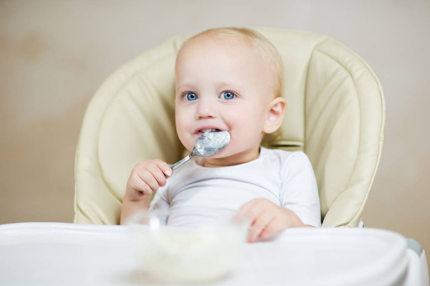 mignonne bébé fille dans une chaise d'alimentation tient une cuillère dans sa bouche et sourit
 - Photo, image