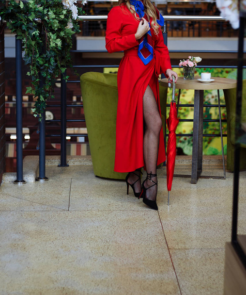 дівчина в червоному плащі в ажурних колготках, сидить в кафе над чашкою кави, чекаючи на зустріч
 - Фото, зображення
