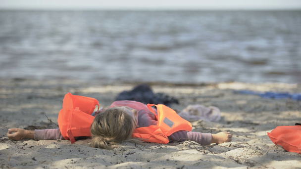 Niña con chaleco salvavidas tumbada en la orilla del mar, sobreviviente de una inundación natural
 - Metraje, vídeo