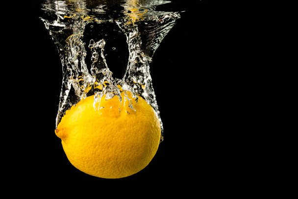 Свежий желтый лимон в воде плеск на черном фоне с большим количеством пузырьков воздуха
. - Фото, изображение
