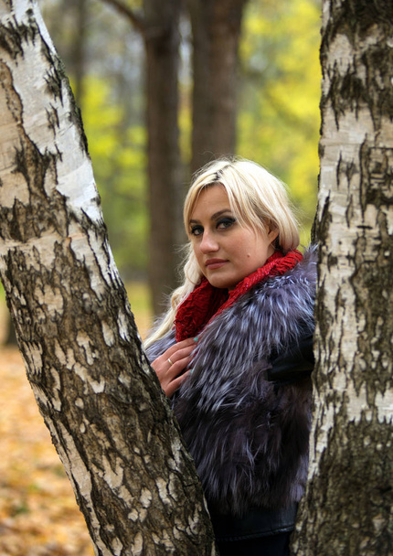 2017.10.21, Moscow, Russia. A young attractive woman wearing fur black jacket standing by the tree. Walking around autumn park. - Foto, Bild