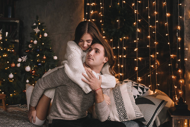 Couple on the bed in the bedroom. Dark interior. New Year's and Christmas. Hugs and kisses. Love. White sweater and high socks. Romantic meeting. A date lovers. - Photo, Image
