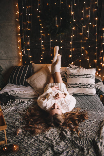 Couple on the bed in the bedroom. Dark interior. New Year's and Christmas. Hugs and kisses. Love. White sweater and high socks. Romantic meeting. A date lovers. - Zdjęcie, obraz