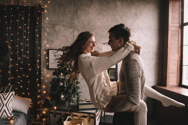 Couple on the bed in the bedroom. Dark interior. New Year's and Christmas. Hugs and kisses. Love. White sweater and high socks. Romantic meeting. A date lovers. - Foto, Bild