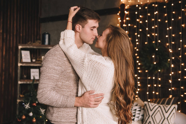 Couple on the bed in the bedroom. Dark interior. New Year's and Christmas. Hugs and kisses. Love. White sweater and high socks. Romantic meeting. A date lovers. - Valokuva, kuva