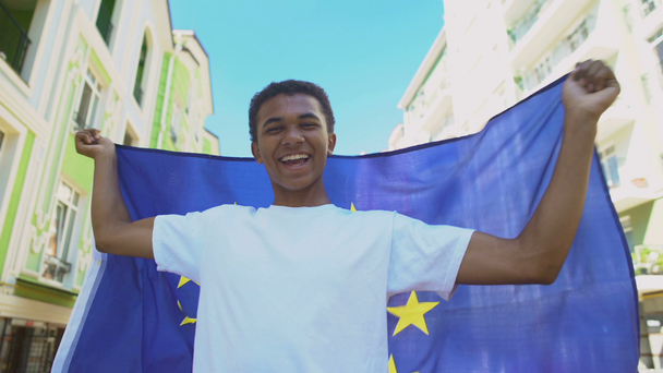 Iloinen sekarotuinen nuori mies heiluttamassa Euroopan unionin lippua ulkona, vapausmarssi
 - Materiaali, video