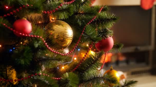 Closeup 4k imagens de árvore de Natal decorado com bugigangas, guirlandas e luzes para celebrar o Ano Novo contra lareira em chamas na sala de estar. Tiro perfeito para celebrações de inverno e feriados
 - Filmagem, Vídeo
