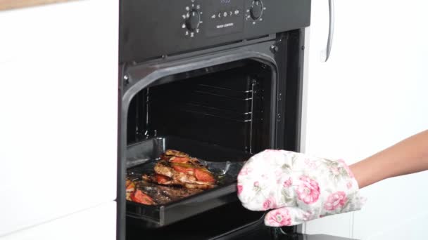 Vrouwelijke handen met handschoenen die de bakpan met vis uit de verwarmde oven krijgen. kookproces - Video