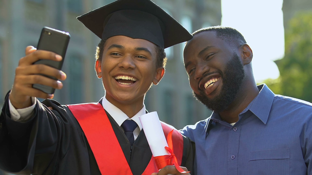 Feliz adolescente emocional em vestido magisterial e pai fazendo graduação selfie
 - Filmagem, Vídeo
