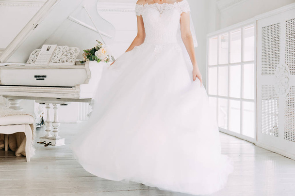 Привлекательная невеста в свадебном платье с длинной полной юбкой, белым фоном, танцами и улыбкой
 - Фото, изображение